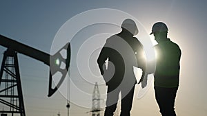 oil production. two silhouette workers work as a team next to an oil pump. business oil production production concept
