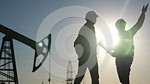 oil production. two silhouette workers work as a team next to an oil pump. business oil production production concept