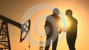 oil production. two silhouette workers work as a team next to an oil pump. business oil production production concept