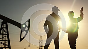 Oil production. Two silhouette workers work as a team next to an oil pump. Business oil production production concept