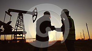 oil production. two workers a work next to an oil pump at sunset silhouette. industry business oil production concept