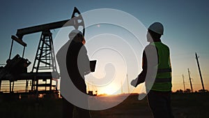 oil production. two workers a work next to an oil pump at sunset silhouette. industry business oil production lifestyle