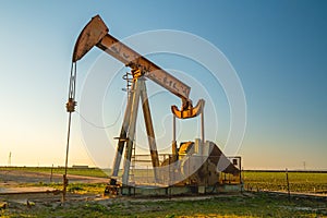 Oil pump and agricultural field at sunset.