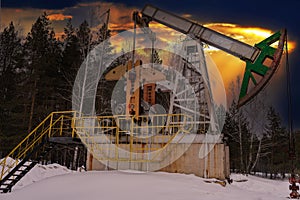 Oil pump jack winter working. At the orange sunset dawn of the sky with clouds. Oil rig energy industrial machine for petroleum in