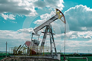 Oil pump tower in the field with green grass with blue cloudy sky