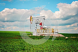 Oil pump tower in the field with green grass with blue cloudy sky