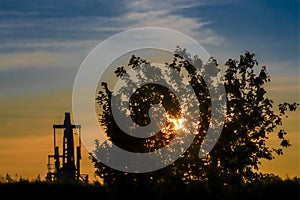 Oil pump and tree at sunset in sun. Gold and blue.