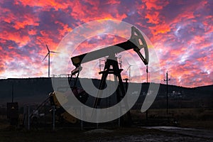 Oil pump and wind turbines against incredible purple sunset sky