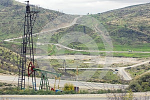 Oil pumps at large oilfield over mountain range. An oil well servicing rig sets up in mountainous country.