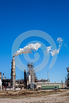 Oil refinery plant with chimney blowing smoke against a clear blue sky.