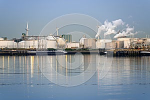 Oil refinery with smokestacks belching out white smoke in a harbour at dusk