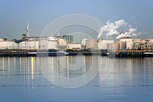 Oil refinery with smokestacks belching out white smoke in a harbour at dusk photo