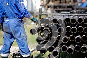 Oil rig drill pipes stacked with oil industry workers in the background. Oil and gas industry. Crude oil pump jack on an oil field