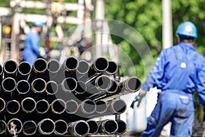 Oil rig drill pipes stacked with oil industry workers in the background. Oil and gas industry. Crude oil pump jack on an oil field