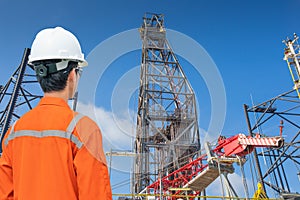 Oil rig worker wearing personal protective equipment looking at drilling rig while in operation for well completion activity
