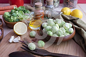 Oil, salt and spices on the board, peeled and washed Brussels sprouts lie in a wooden bowl, next to wooden dishes