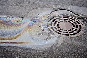 The oil spill on the asphalt road is seeping into the storm drain, causing water pollution.