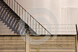 Oil storage tank stairs behind a concrete wall with a barbed wire