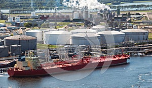 Oil tanker moored an oil terminal with fuel storage silos in an industrial port