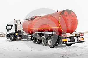 Oil tanker truck with a red tank semi-trailer on a winter road