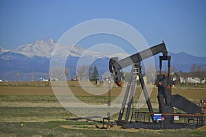 Oil well, pump jack with snow capped mountains