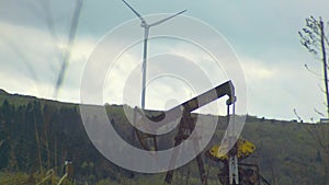 Oil well with pump jack and Wind power plant on the mountain in background