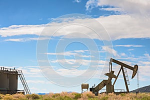 Oil Well And Tank Against Mountains and Blue Cloudy Sky