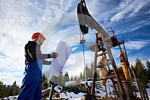 Oil worker standing in the oilfield next to a pump jack with a big paper