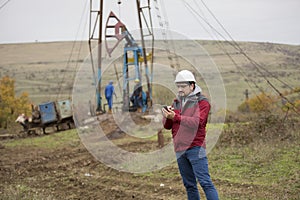 Oil worker in uniform and helmet, with mobile phone.