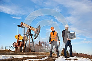 Oil workers standing on territory of oil field with pump jack.