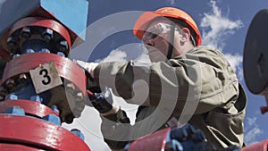 Oilman in orange helmet and protective glass opening or closing valve of wellhead to shut off well. Decline in oil