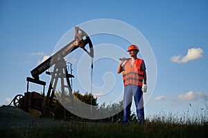 Oilman in overalls standing against oil pump jack.