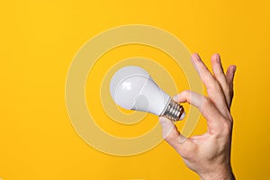 Ok gesture closeup hand holding white led lighting bulb against a yellow wide background banner with copyspace. concept