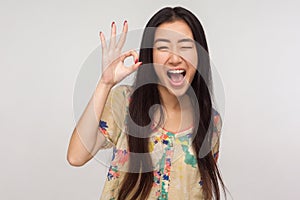 Ok I got it! Playful delighted asian girl with brunette hair in summer blouse winking joyfully and showing okay gesture