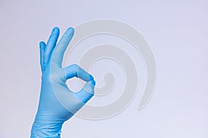 Ok sign is showed by left man hand in a blue medical glove on a white background. Okay photo