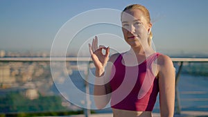 Okay! Close-up. sporty young girl runner approvingly shows ok gesture. Girl with wireless headphones. 4K
