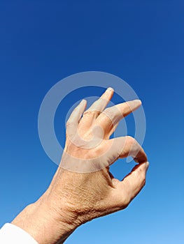 The okay gesture. is to unite the thumb and the index finger and the other straight ones with blue sky photo