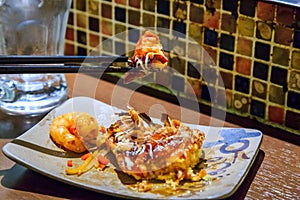 Okonomiyaki , Japanese fried pizza on chopsticks, selected focus.
