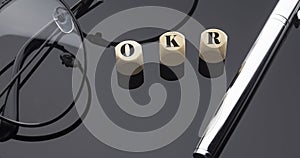 OKR concept, words on wooden blocks on the black background with pen and glasses