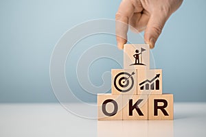 OKR Objectives, Key and Results wooden cube blocks on blue background. Business target and drive business and performance.
