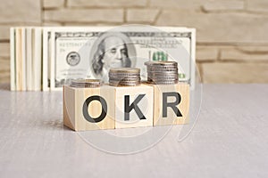 OKR - text on wooden blocks and US dollar bills and coins background. business to business concept