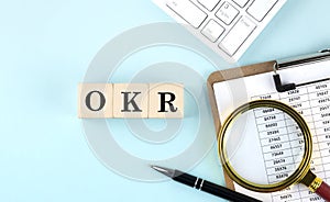 OKR word on wooden cubes on a blue background with chart and keyboard