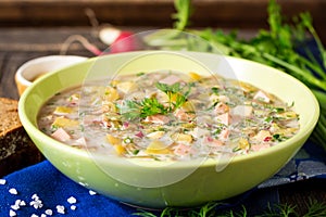 Okroshka. Traditional Russian summer cold soup with sausage, vegetables and kvass in bowl on wooden background.