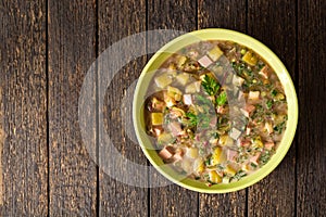 Okroshka. Traditional Russian summer cold soup with sausage, vegetables and kvass in bowl on wooden background.