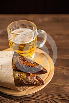 Oktoberfest holiday concept. Beer, smoked fish, chips on a wooden textural background in a dark key. Beer in a glass, fish in pape