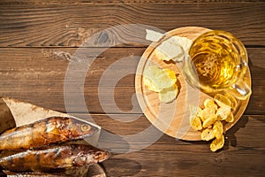 Oktoberfest holiday concept. Beer, smoked fish, chips on a wooden textural background in a dark key. Beer in a glass, fish in pape