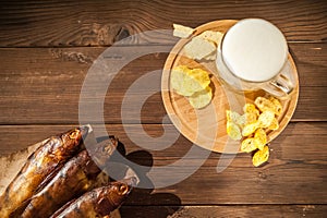 Oktoberfest holiday concept. Beer, smoked fish, chips on a wooden textural background in a dark key. Beer in a glass, fish in pape