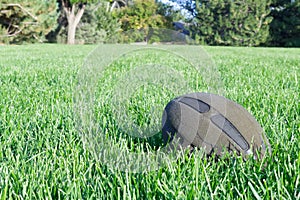 Old abandoned american football ball at field alone laying in green grass in park. Outdoors sports concept. Horizontal