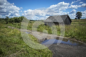 Old abandoned barn and country road with puddle