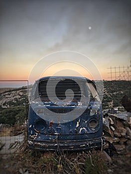 An old abandoned beetle van in Naxos during sunset, with fire smoke on the background